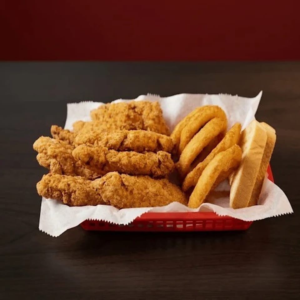 Basket of crispy fried chicken tenders, onion rings, and thick-cut fries on a paper-lined tray.