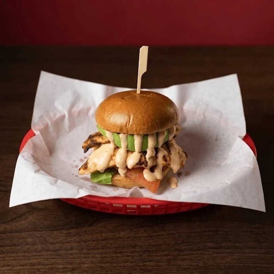 Loaded grilled chicken sandwich with creamy sauce, lettuce, and pickles on a paper-lined red basket.