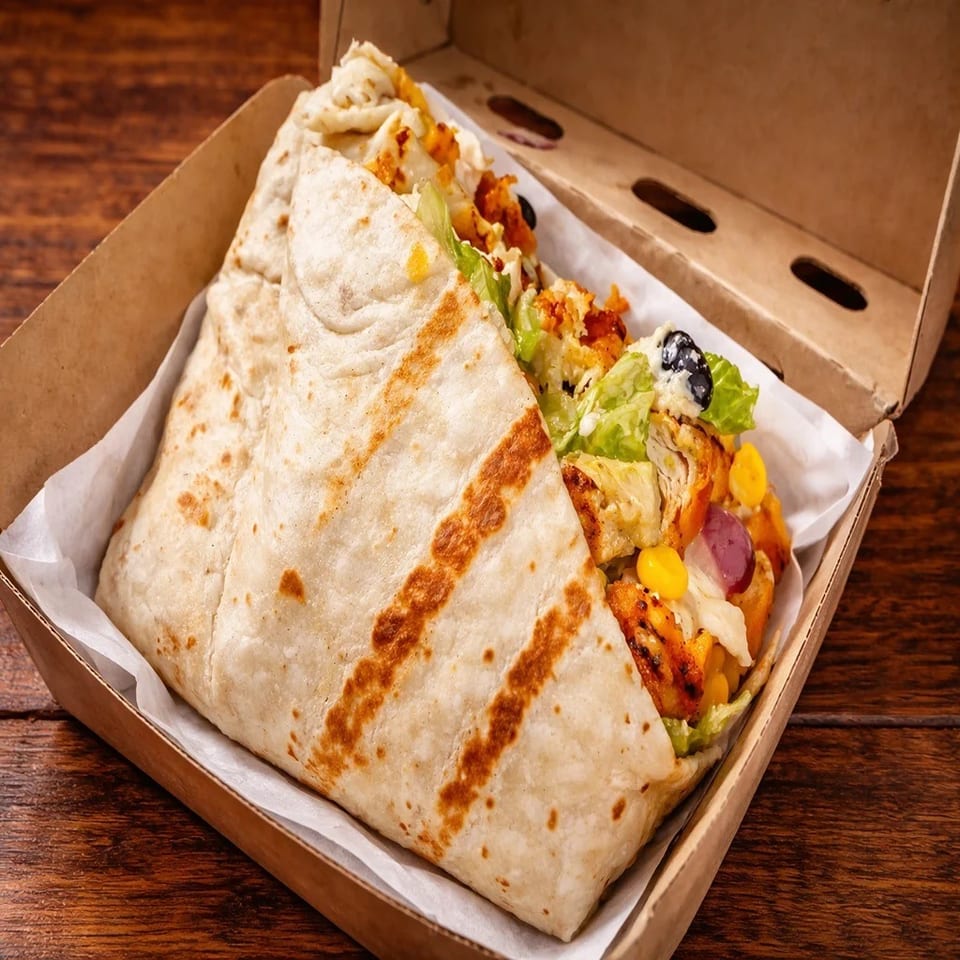 Two grilled chicken wraps filled with lettuce, vegetables, olives, and sauce in an open cardboard takeaway box.