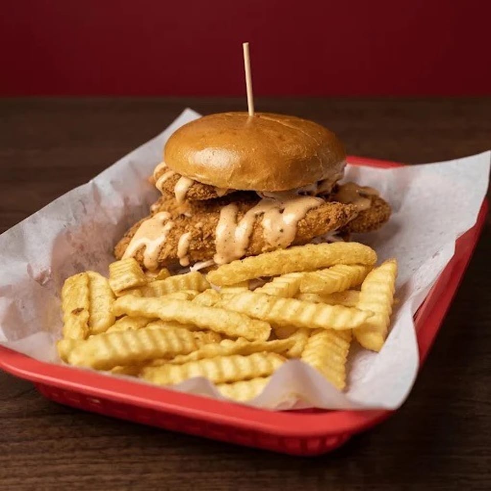Crispy fried chicken sandwich with creamy sauce and crinkle-cut fries served in a red basket.